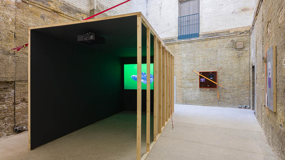 A photo of a large wooden structure with a screen inside in an exposed brick gallery space