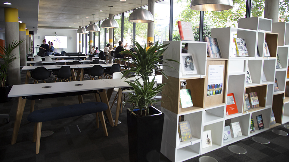 A bookshelf and some tables next to plants in the Library